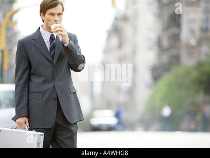 Imprenditore in strada, mangiare in viaggio Foto Stock