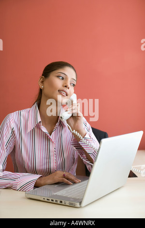 Imprenditrice parlando al telefono mentre utilizzando laptop Foto Stock