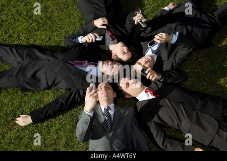 Imprenditori utilizzando i loro telefoni cellulari mentre posa in erba Foto Stock