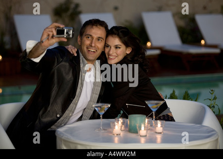 Paio di scattare le foto di se stessi godendo bevande a lume di candela da piscina Foto Stock