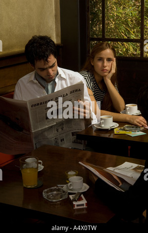 L'uomo leggendo un giornale come annoiato ragazza seduta accanto a lui in cafe Foto Stock