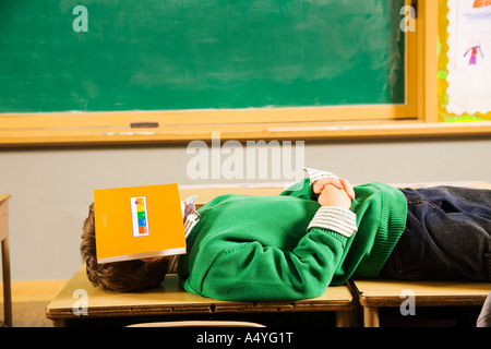 Ragazzo posa su banchi con libro sulla faccia Foto Stock