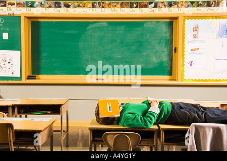 Ragazzo posa su banchi con libro sulla faccia Foto Stock