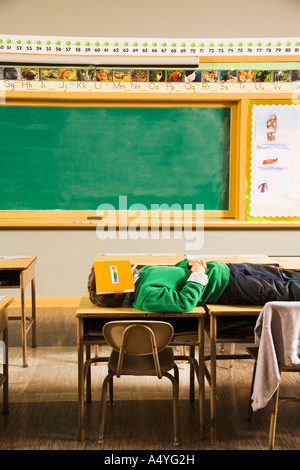 Ragazzo posa su banchi con libro sulla faccia Foto Stock