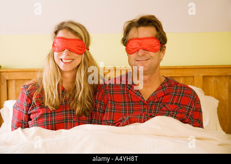 Giovane seduto a letto indossando maschere per occhi Foto Stock