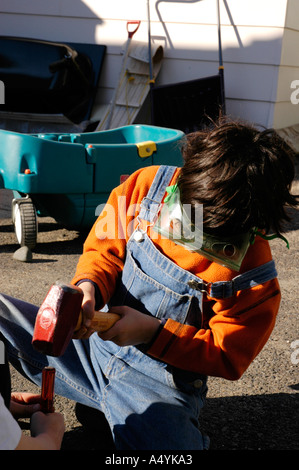 Ragazzo giovane sette 7 giocando con il martello cercando di rompere una roccia e indossare occhiali di sicurezza Foto Stock