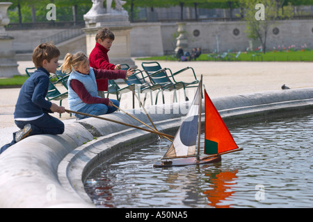 Bambini che giocano con un modello di barca su un lago in giardini Tuileries Parigi Francia Foto Stock