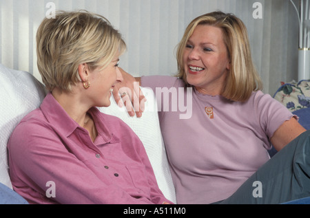 Due felice giovane biondo donne chat sul divano di casa Foto Stock