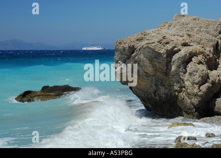 Onde che si infrangono sulle rocce su una spiaggia vicino alla città di Rodi in Grecia con una delle isole greche traghetto all'orizzonte Foto Stock