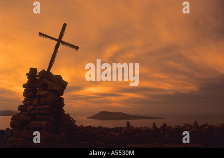 Croce su cairn di pietra sulla cima dell'isola Taquile al tramonto, isola di Amantani in lontananza, lago Titicaca, Perù Foto Stock