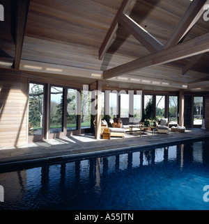 Grande piscina interna nel paese fienile conversione con confortevole area salotto e vista del giardino attraverso le finestre Foto Stock