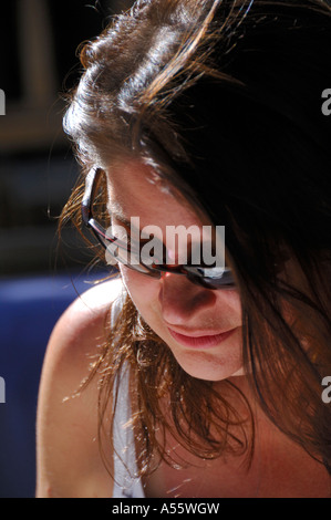 Donna seduta nel sole con occhiali da sole concentrandosi sulla scrittura Foto Stock