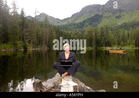 Imprenditrice seduta al lago con il computer portatile Foto Stock