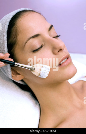 Giovane donna con maschera facciale applicata con il make-up spazzola, gli occhi chiusi, close-up Foto Stock