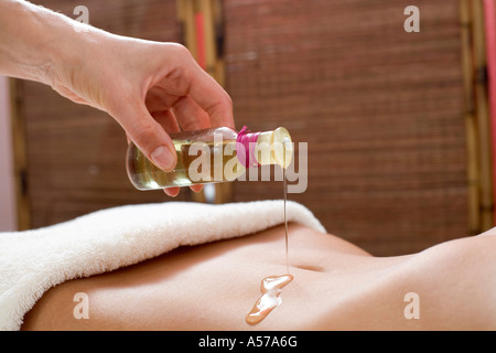 Massaggiatore versando olio sulla donna di pancia, metà sezione, close-up Foto Stock