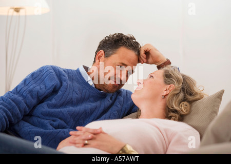 Coppia matura sdraiato sul divano, faccia a faccia sorridente Foto Stock