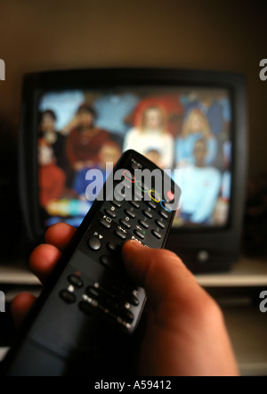 Mano che tiene il telecomando del TV con televisore in background Foto Stock
