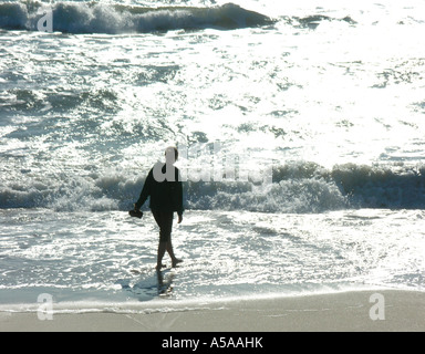 Giovane donna casualmente a piedi sulla spiaggia in acqua poco profonda Foto Stock