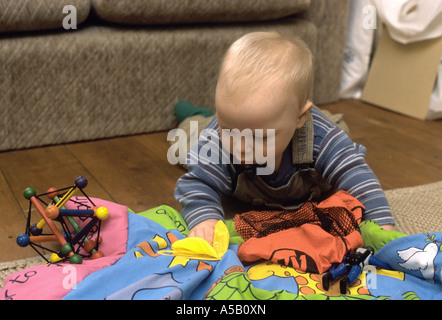 Sei mese baby boy sul suo stomaco esplorando i giocattoli sul pavimento Foto Stock