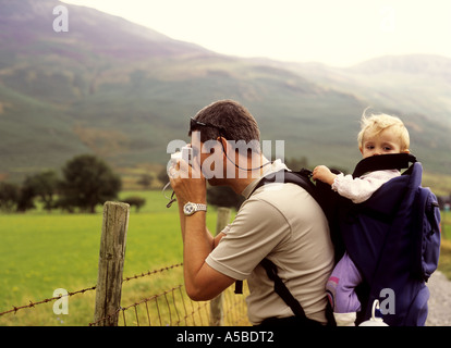 Padre in vacanza a Buttermere nel distretto del lago in UK scattare fotografie con la sua bimba in uno zaino Foto Stock