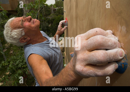 Uomo anziano salendo su un artificiale di arrampicata verticale con scalatore holding afferra e guardare avanti per il prossimo grip Foto Stock