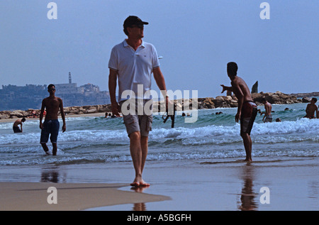 Un uomo a camminare sulla spiaggia con Jaffa in background di Tel Aviv Foto Stock