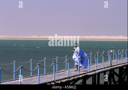 Donna in abiti tradizionali che guarda all'Oceano Atlantico e la costa da Pier, Mauritania, Africa Foto Stock