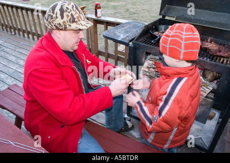 Papà aiutando figlio squish riscaldata marshmallow e cioccolato tra graham cracker per rendere un smore. Clitherall Minnesota USA Foto Stock