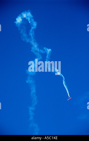 Piccolo aereo rosso di coda di fumo bianco di eseguire acrobazie aeree contro un profondo cielo blu Foto Stock