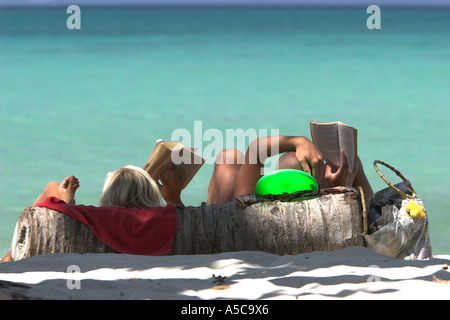 Paio di leggere sulla spiaggia tropicale in appoggio sulla palma da cocco log Ao Lo Dalam beach Phi Phi Island Thailandia Foto Stock