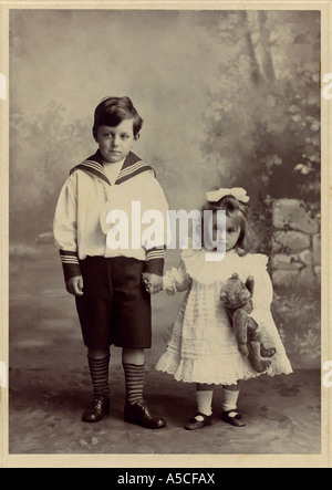 Studio foto ritratto di Edwardian ragazzo e una ragazza con un orsacchiotto di peluche, UK. circa 1910 Foto Stock