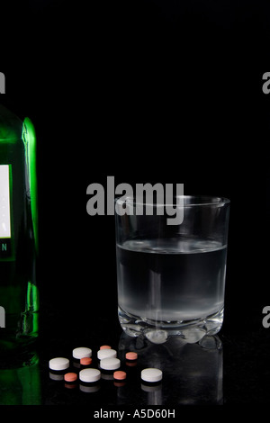 Bicchiere di gin o acqua con un carico di pillole a simboleggiare la dipendenza del suicidio e overdos o forse solo imprudente mescolare Foto Stock