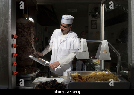 Un venditore taglia la carne su uno spiedino in un Shawarma anche ortografato shawurma o shawerma grill bistro a Gerusalemme Israele Foto Stock