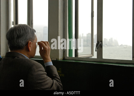 Uomo anziano guardando attraverso le finestre verso il mare di edifici di Hong Kong Island dalla penisola di Kowloon, Cina Foto Stock