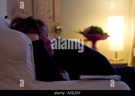 Le donne bianche di profilo sulla crema sedia facile guardare la TV anche in condizioni di scarsa illuminazione con telecomando sul braccio della sedia Foto Stock