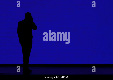 Silhouette di un imprenditore parlando a un telefono cellulare di fronte a un gigante blu dello schermo video Foto Stock