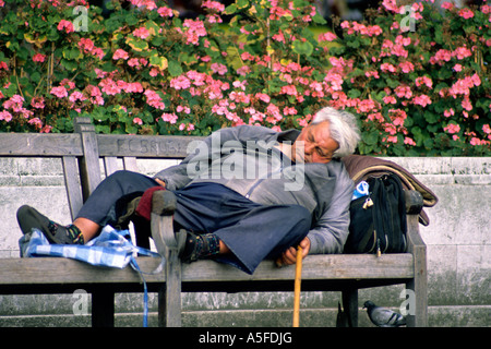 Un senzatetto uomo dorme su una panchina nel parco in London Inghilterra England Foto Stock