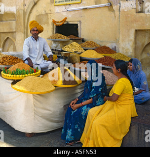 Tre donne alla ricerca a livello locale turbaned uomo seduto zampe trasversale nella sua stalla dei cestelli circolari di spezie al Forte Amber India Foto Stock