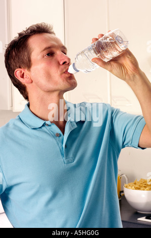 Uomo in cucina di bere dalla bottiglia di acqua Foto Stock