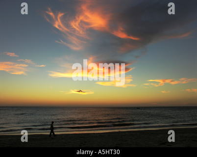 Uomo a camminare sulla spiaggia al tramonto spettacolare nuvole di post-incandescenza Foto Stock