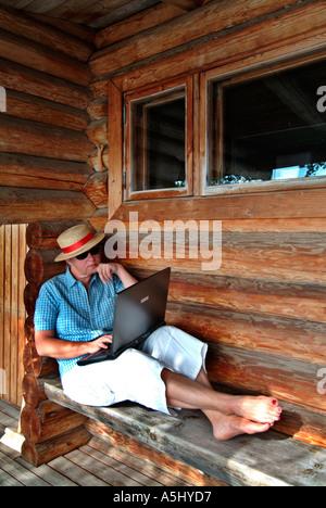 Donna che lavorano con un pc portatile seduti sulla veranda di una sauna cot sul lungolago in Finlandia Foto Stock