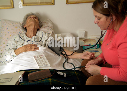Una donna anziana è sdraiato torna nel suo letto avente la sua pressione del sangue preso da un infermiere visitando la sua casa Foto Stock