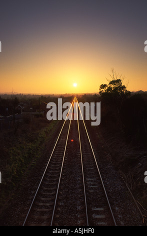 Binario ferroviario conduce direttamente verso il sole al tramonto sul lontano orizzonte in Bradford Abbas village contea di Dorset England Regno Unito Foto Stock