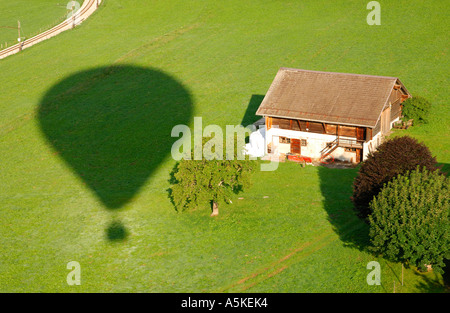 Ombra di una mongolfiera tra i binari ferroviari e una fattoria vista aerea svizzera Foto Stock