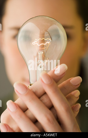 Donna che mantiene la lampadina di luce nella parte anteriore del viso Foto Stock