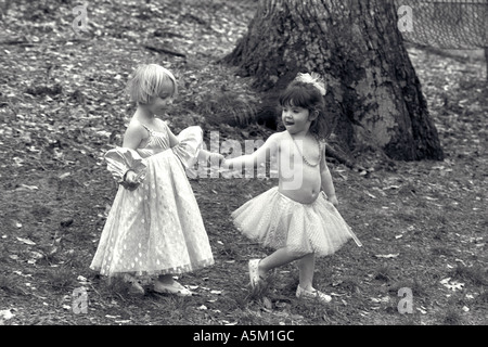 Due tre anni di ragazze che indossano costumi di fata camminare la mano e la mano dolcemente attraverso i boschi di questa immagine in bianco e nero Foto Stock