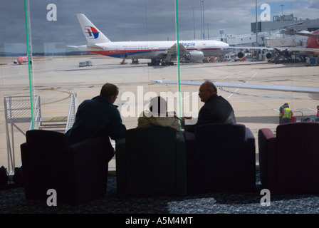 I passeggeri in attesa di partenza all'Aeroporto Internazionale di Melbourne con una Malaysian Airlines Boeing 777 200 in background Foto Stock