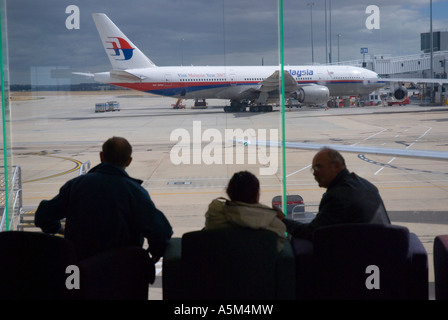 I passeggeri in attesa di partenza all'Aeroporto Internazionale di Melbourne con una Malaysian Airlines Boeing 777 200 in background Foto Stock