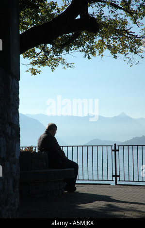 Un vecchio uomo seduto in ombra di alberi che si affaccia sul lago di como Foto Stock