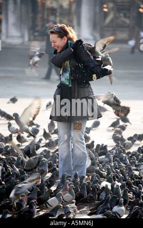 Una giovane donna ride come piccioni atterrare su di lei in Piazza San Marco a Venezia Italia Foto Stock